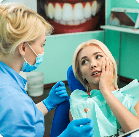 Woman holding side of her jaw in pain while talking to dentist