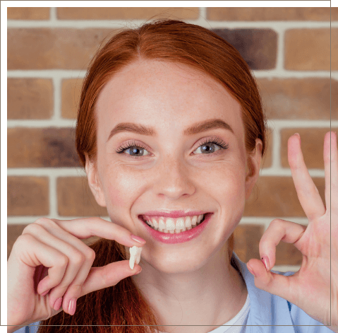 Smiling woman holding tooth after tooth extraction in Oklahoma City
