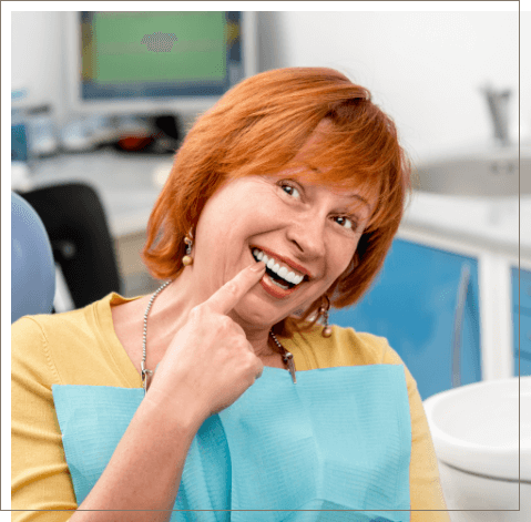 Redheaded dental patient pointing to her smile with dental implants in Oklahoma City