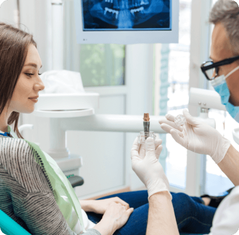 Dentist showing a dental implant to a young woman in dental chair