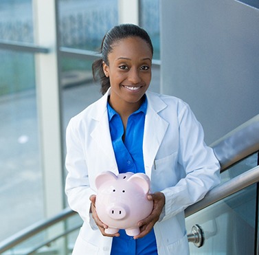 Dentist smiling while holding piggy bank in office stairwell