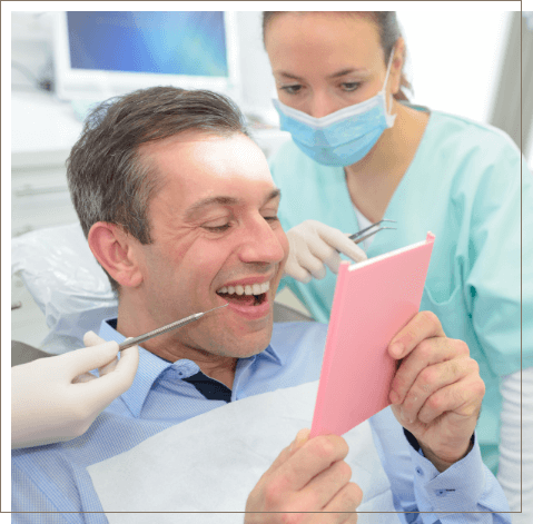 Dental patient admiring his smile in mirror after replacing missing teeth